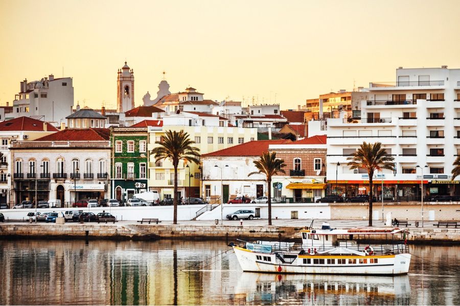 Een foto van een haven in de Algarve, genomen bij zonsondergang, met een klein bootje op de voorgrond. 