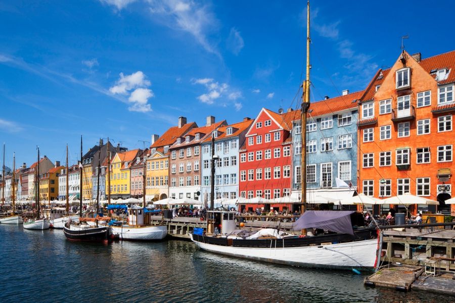 Een foto van de felgekleurde gebouwen van Kopenhagen in de haven, met kleine zeilbootjes die aan de kade liggen. 