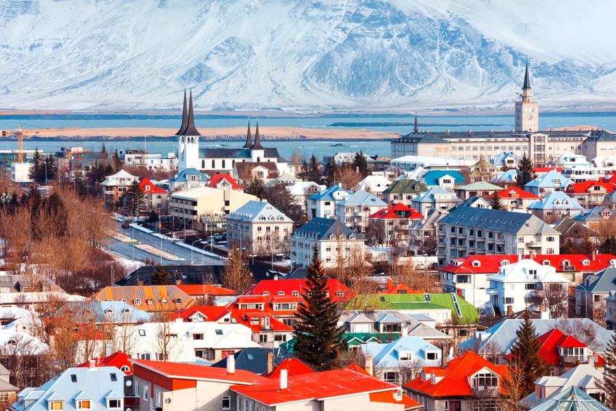 Een foto van felgekleurde daken in Reykjavik, genomen met de rand van het water op de achtergrond en een besneeuwde berg in de verte.