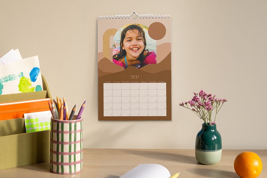 Een gepersonaliseerde kalender met de maand september en een foto van een jong meisje hangt boven een bureau met een pennenbakje, een vaas met bloemen en een organizer met knutsel- en schoolspullen, ter illustratie van albelli's tip om een rustige werkplek te creëren voor het schooljaar.