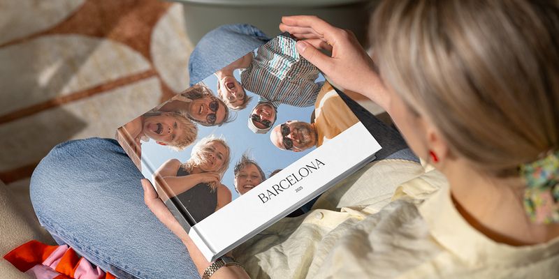 Een vrouw kijkt naar een fotoboek met de titel 'Barcelona', met een foto van veel lachende gezichten van familie die naar beneden kijken in de camera, ter illustratie van albelli's gids voor het maken van een groepsfotoboek.