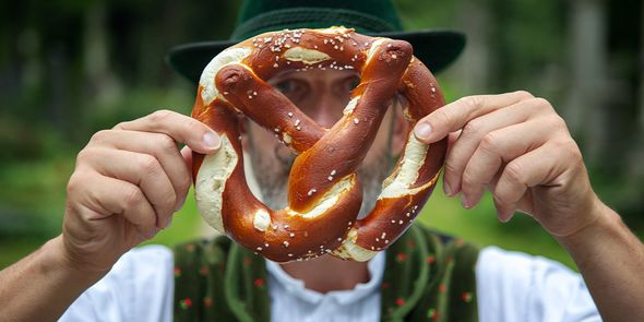 Een man in traditionele Beierse kledij houdt een grote pretzel voor zijn gezicht, ter introductie van albelli's gids over de beste Oktoberfeeststeden in Europa.