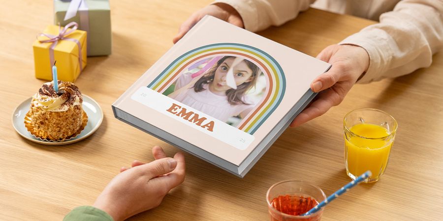 Een fotoboek verjaardag voor Emma wordt over een tafel met taart en cadeau geschoven, als voorbeeld voor verjaardag fotoboek maken of een fotoalbum verjaardag bij albelli.