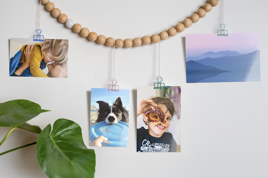 Creatieve manieren om albelli foto afdrukken te tonen, met familiefoto’s van een hond, een kind met een donut en een landschap die met clips aan een kralenslinger hangen, als inspiratie voor foto afdrukken en online foto’s bestellen.
