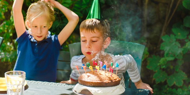 Een jongen blaast de kaarsjes uit op zijn verjaardagstaart, als inspiratie voor albelli kinderfeestje ideeën en een onvergetelijk kinderfeestje.