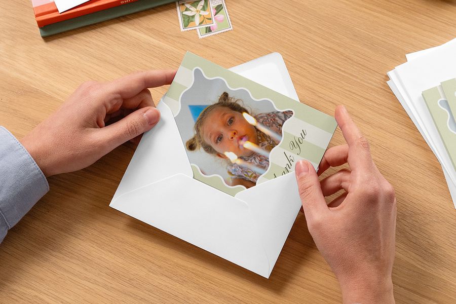 Handen stoppen een gepersonaliseerde bedankkaart van een kind in een envelop, als inspiratie voor albelli kinderfeestje ideeën en persoonlijke bedankkaartjes na een kinderfeestje.