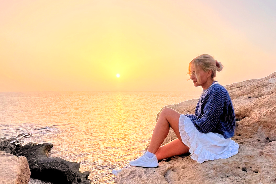 Een vrouw die op rotsen aan zee zit met de ondergaande zon achter haar, als illustratie van hoe het gouden uur zorgt voor warme en prachtige foto’s.