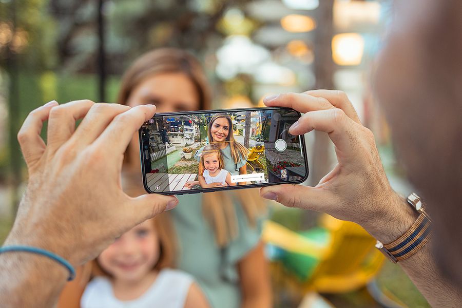 A hand holding a phone captures a smiling mother and daughter in bright sunlight, illustrating how to take photos in bright sunlight using your phone.