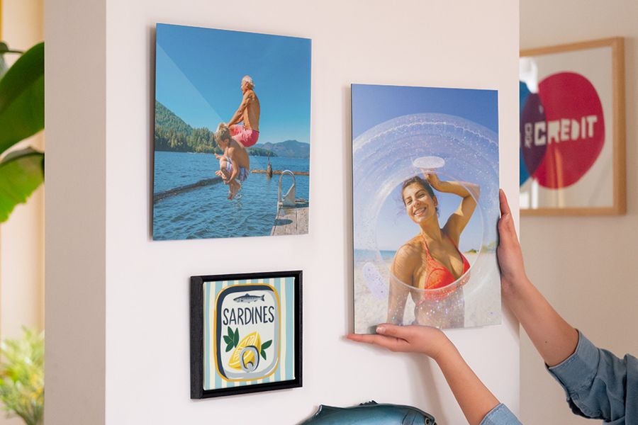 Een wand met gepersonaliseerde albelli wanddecoratie toont een lachende vrouw op het strand, een man en jongen die in zee springen en een illustratie van een blik sardines, als inspiratie voor zomer decoratie in huis en interieur zomer decoratie.