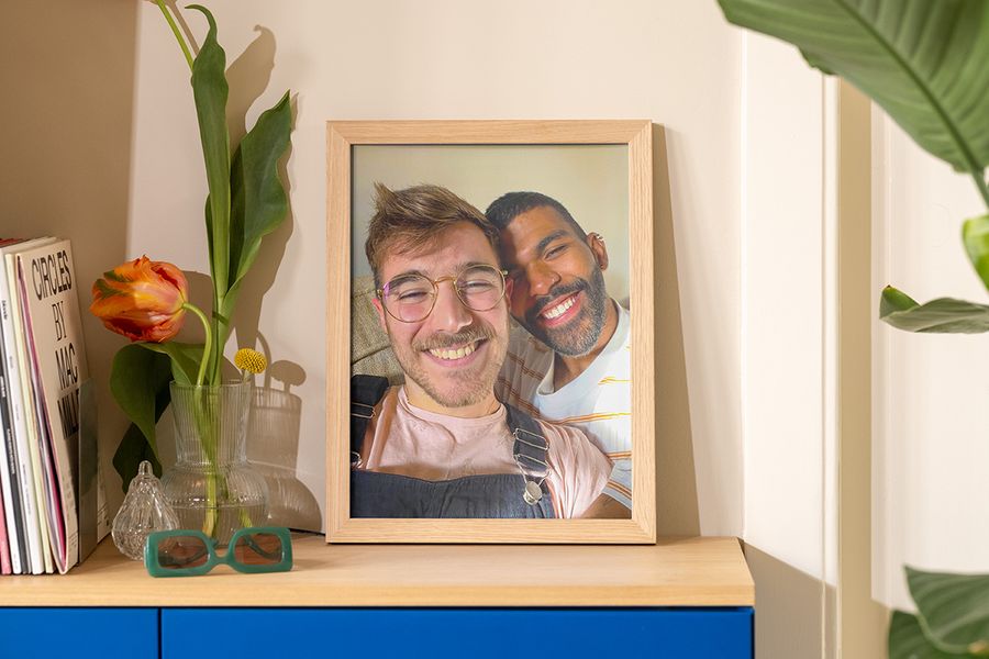 Een ingelijste foto van twee mannen die in de zon een selfie maken staat op een dressoir naast een vaas, een zonnebril en een tijdschrift, als inspiratie voor zomer decoratie woonkamer en interieur zomer decoratie.