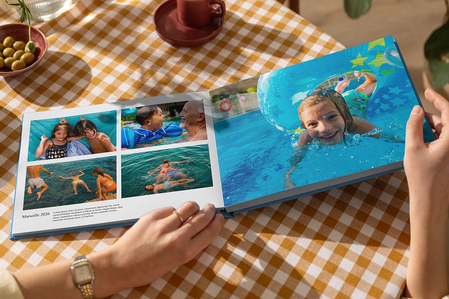 Een open albelli vakantie fotoboek toont zomerse familiefoto’s van spelende mensen in het water, met één paginagrote foto en een andere pagina met de titel Marseille 2026, een bijschrift en beschrijving, als illustratie van hoe tekst een gepersonaliseerd reisfotoboek tot leven brengt.