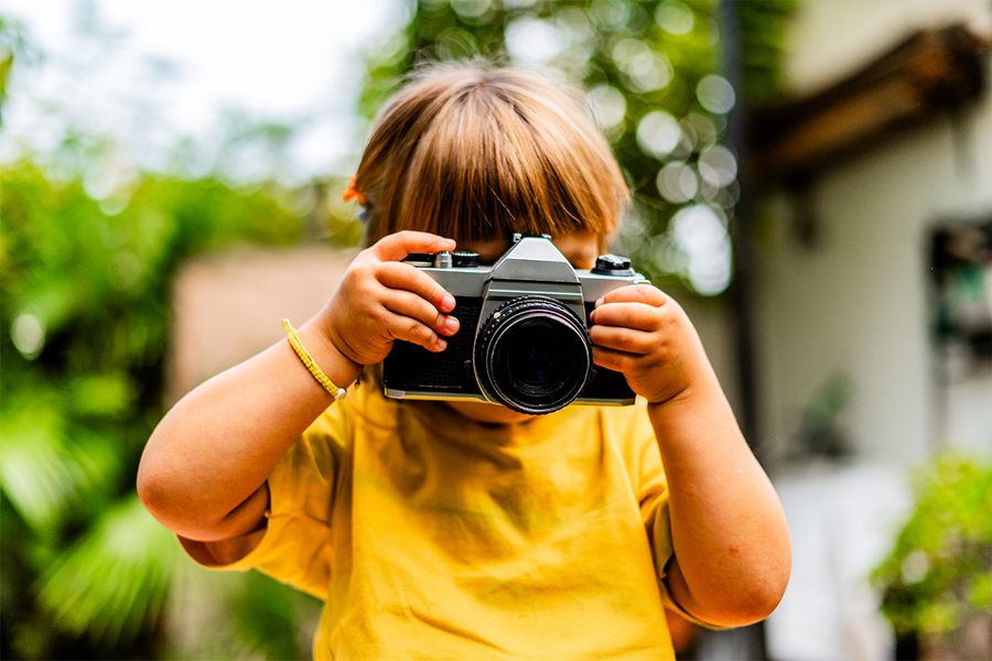 Een jong meisje maakt foto's met een camera, passend bij albelli's tips voor een creatieve vakantie thuis.