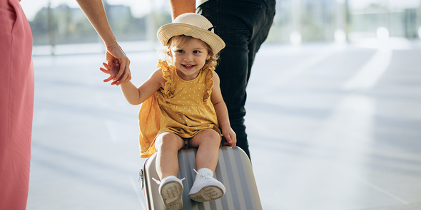 Een klein meisje zit op een koffer die wordt voortgetrokken, een speels beeld van vakantie met kinderen en gezinsreizen met albelli.