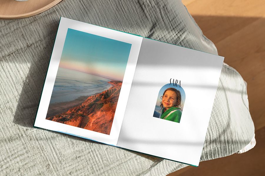 Een geopend fotoboek toont op één pagina een prachtig landschap en op de andere een foto van een meisje met het bijschrift 'Sara', ter illustratie van albelli's Artisan Masking-ontwerp met speelse kaders geïnspireerd op vintage ansichtkaarten en postzegels.