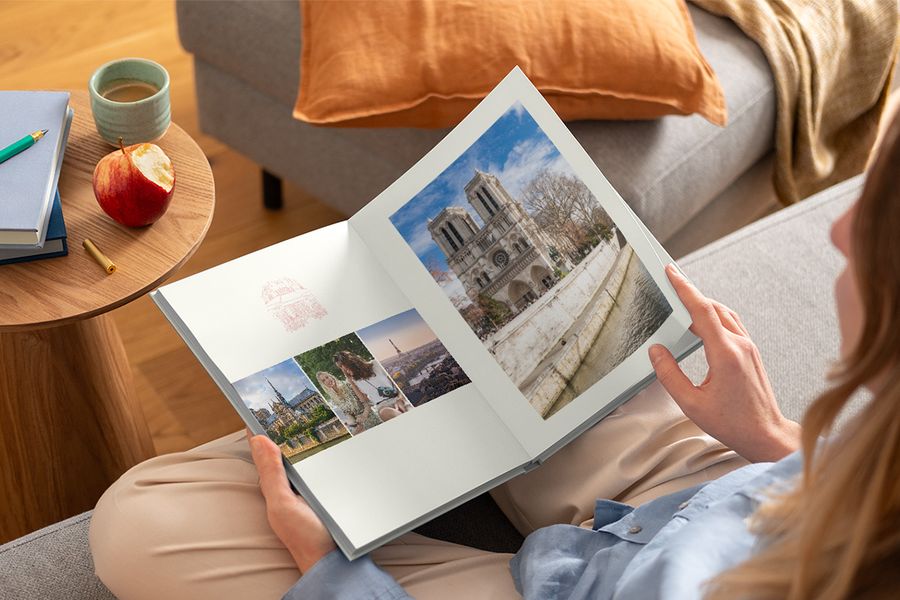 Een vrouw houdt een geopend fotoboek op schoot met verschillende reisfoto's, ter illustratie van albelli's Graphic Getaways-ontwerp geïnspireerd op vintage reisposters en geïllustreerde stadsplattegronden.