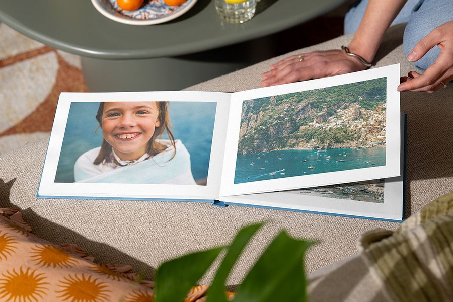 Een geopend fotoboek toont op één pagina een lachend meisje bij de zee en op de andere pagina een strandlandschap, ter illustratie van albelli's Holiday Escape-ontwerp met meeslepende foto's over de volledige pagina.