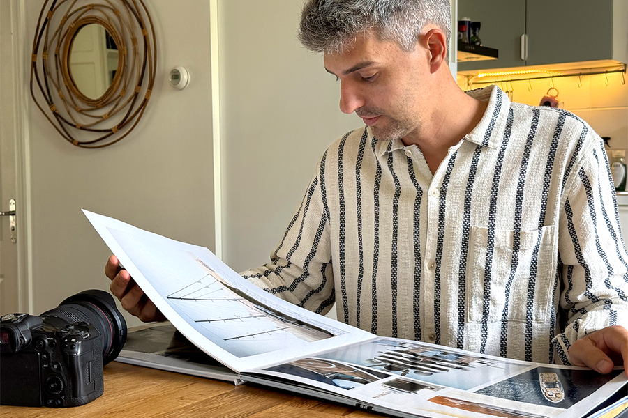 Charl van Rooy zit in zijn keuken en kijkt naar zijn geopende portfolio, met zijn camera naast hem op de tafel, ter illustratie van albelli's gids voor het maken van een fotografieportfolio als fotoboek.