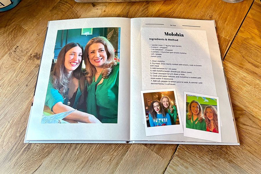 Een spread uit Sarah's gepersonaliseerde kookboek toont een recept voor molohia, vergezeld van familiefoto's in plaats van een foto van het gerecht, ter illustratie van albelli's tip om persoonlijke foto's toe te voegen die een kookboek écht betekenisvol maken.