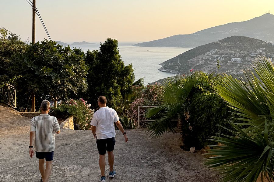 Two men walk down a hill surrounded by plants towards the sea in Kalkan, capturing the charm of a Turkish September holiday on the Turquoise Coast.