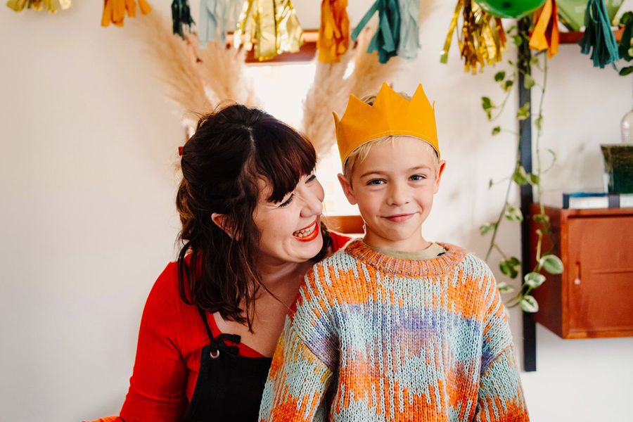 Een lachende jonge jongen draagt een verjaardagskroon terwijl een oudere vrouw naar hem glimlacht, ter illustratie van albelli's ultieme checklist voor de verjaardagsfotoshoot.