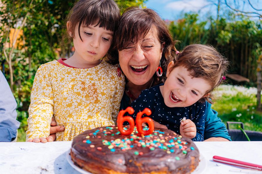 Een vrouw glimlacht naast haar verjaardagstaart met kaarsjes die '66' aangeven, geflankeerd door twee lachende kinderen, ter illustratie van albelli's tips om verjaardagsmomenten met meerdere generaties vast te leggen.