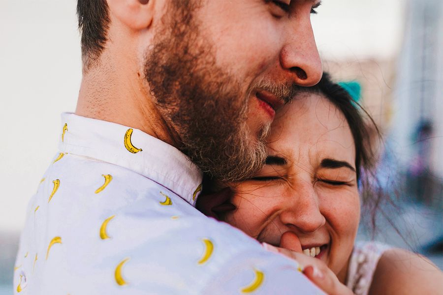 Een koppel omhelst elkaar, waarbij de vrouw glimlacht met haar ogen dicht, ter illustratie van albelli's ideeën voor wat je kunt schrijven in een huwelijksjubileumkaart.