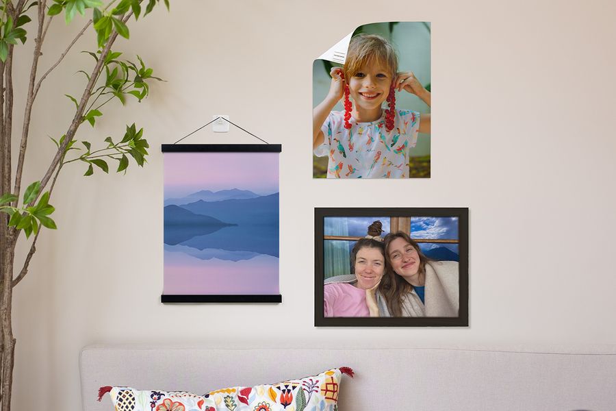 Verschillende albelli-opties voor het ophangen van wanddecoratie worden in huis getoond, waaronder een gepersonaliseerde poster van een jonge jongen die met plakstrips is bevestigd, een gepersonaliseerde landschapsposter opgehangen met een houten hanger en plakhaak, en een ingelijste foto van twee lachende meisjes.