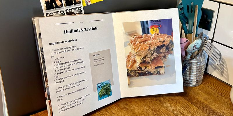 Een geopend gepersonaliseerd kookboek staat in een keuken, met een pot met lepels en keukengerei op de achtergrond, ter introductie van albelli's gids om je eigen kookboek te maken.