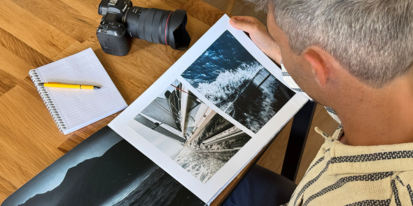 Fotograaf Charl van Rooy kijkt naar zijn portfolio, met zijn camera en een notitieboekje naast hem op de tafel, ter introductie van albelli's gids voor het maken van een fotografieportfolio als fotoboek.
