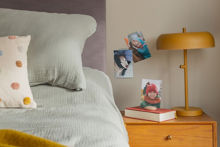 Een selectie familiefotoprints hangt aan de muur naast een bed, ter illustratie van hoe albelli fotoprints een gezellige, persoonlijke toets geven aan een hygge-slaapkamer.