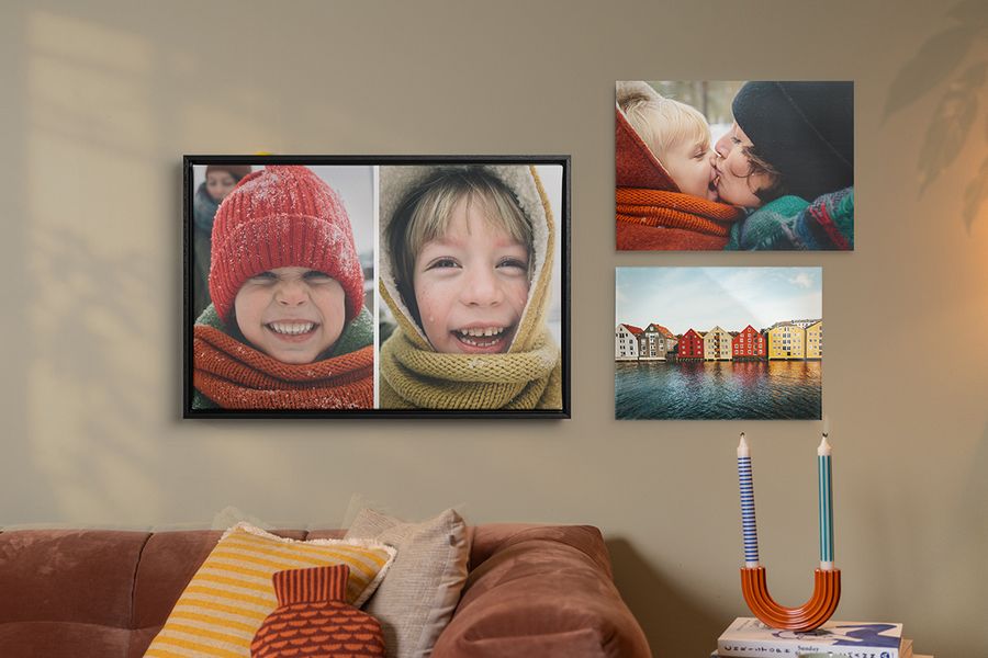 Drie voorbeelden van gepersonaliseerde wanddecoratie hangen boven een bank in een woonkamer, herfstachtige familieprints met lachende kinderen in winterkleding, ter illustratie van hoe albelli wanddecoratie een gezellige hygge-stijl aan je huis geeft.