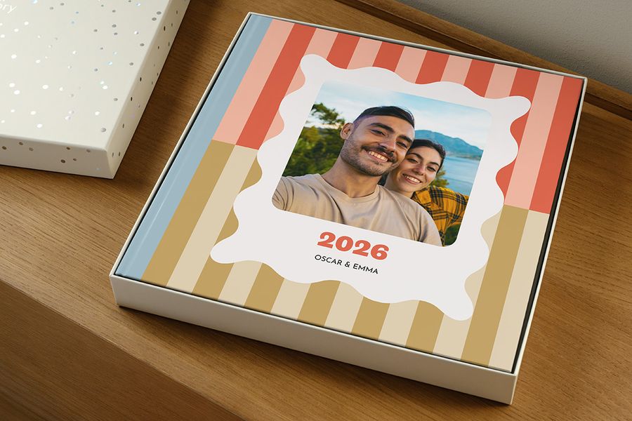Een fotoboek ligt in de cadeaudoos zonder deksel, en lijkt op een jaarboek met het label '2026' en een lachend koppel op de cover, ter illustratie van hoe je de juiste maat presentatiedoos kiest voor je fotoboek.
