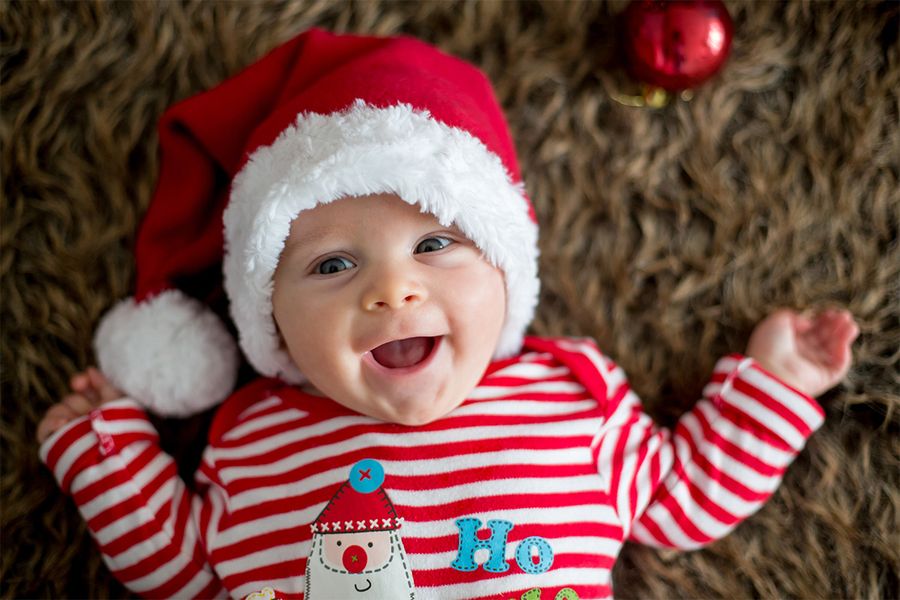 Lachende baby op een kleed met een kerstmuts en een rood-wit gestreept kerstshirt, ter illustratie van albelli’s tips voor sfeervolle kerstfoto’s voor de eerste kerst van een baby.