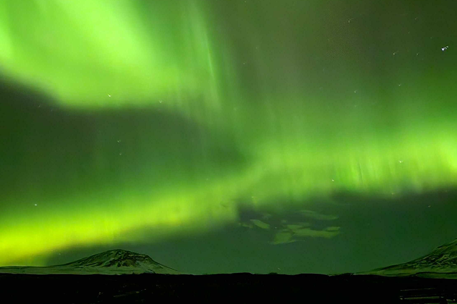 Besneeuwde bergen onder een hemel die door het noorderlicht zeer groen kleurt, ter illustratie van albelli’s tips over waar je noorderlicht kunt zien zonder naar IJsland te gaan.