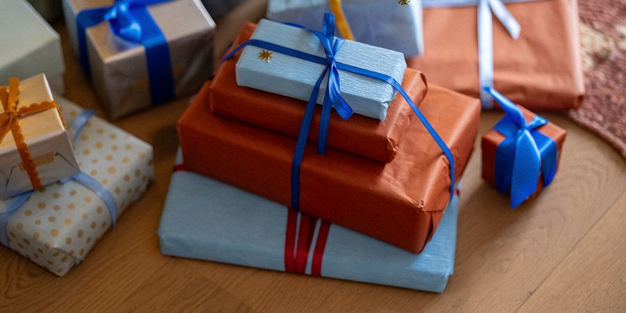Een stapel cadeaus in oranje en lichtblauw papier met blauwe linten op een houten vloer, ter illustratie van albelli’s tips voor black friday kerstcadeaus.