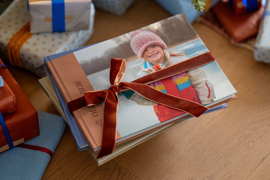Stapel gepersonaliseerde fotoboeken met een bruin fluwelen lint eromheen, met andere ingepakte cadeaus op de achtergrond, ter illustratie van albelli’s tips om een gepersonaliseerd fotocadeau voor kerst voor te bereiden.
