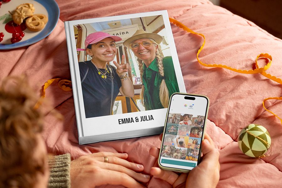 Gepersonaliseerd fotoboek met de titel “Emma and Julia” met een moeder en haar volwassen dochter op de cover, naast de handen van een man die een telefoon vasthoudt om te laten zien hoe makkelijk het is om foto’s te selecteren en een albelli-fotoboek te maken, ter illustratie van albelli’s tips om foto’s van familie en vrienden te verzamelen voor een gepersonaliseerd cadeau.