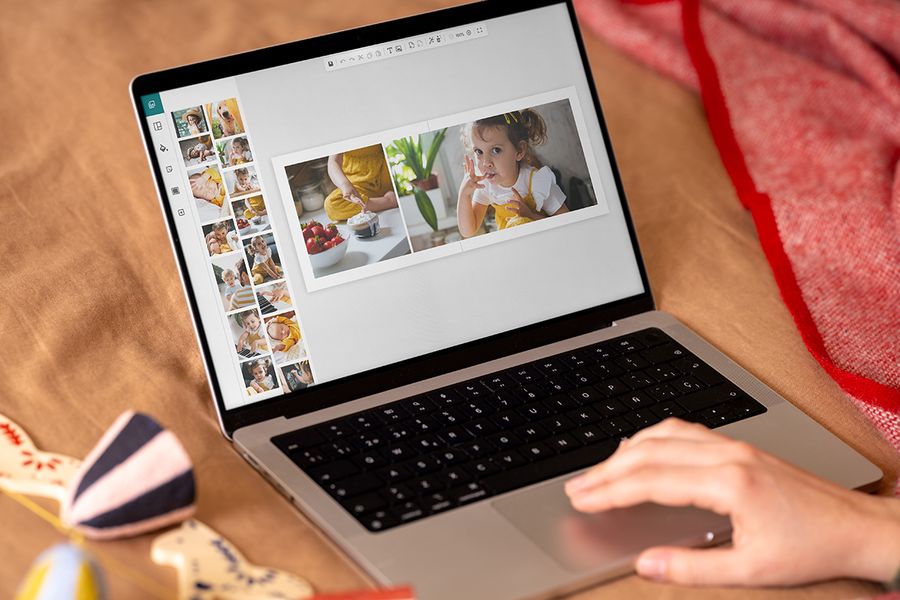Handen achter een laptop met de online editor van albelli, om te laten zien hoe makkelijk het is om een fotoboek te maken als gepersonaliseerd kerstcadeau, ter illustratie van albelli’s tijdlijn om een gepersonaliseerd fotocadeau te maken.