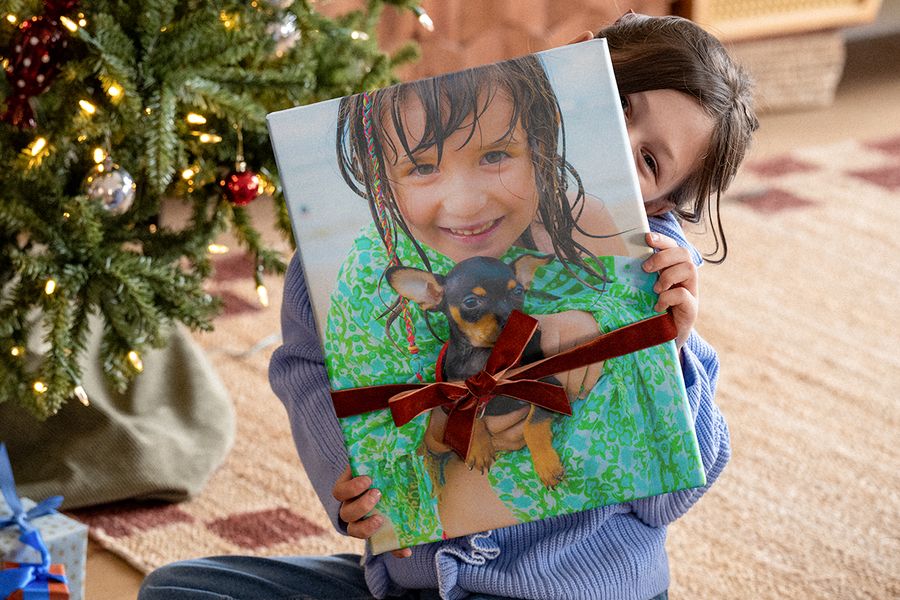 Klein meisje onder de kerstboom met een groot fotoboek met een fluwelen lint eromheen en een foto van haarzelf met een chihuahua op de cover, ter illustratie van albelli’s checklist voor een gepersonaliseerd fotocadeau voor kerst.