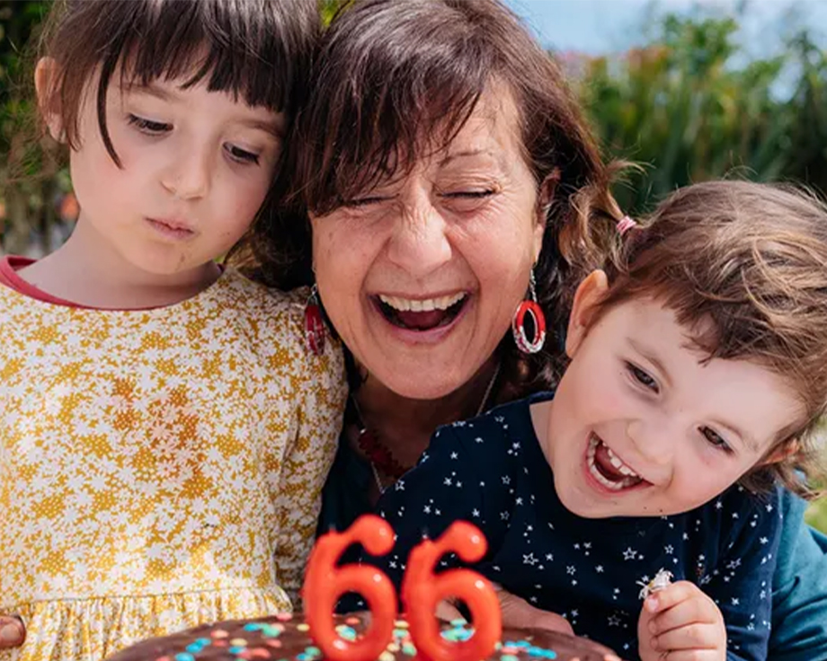 Een oma viert haar 66e verjaardag met haar twee kleinkinderen naast zich en staat op het punt de kaarsjes op haar taart uit te blazen, als inspiratie voor verjaardagscadeaus uit de ultieme verjaardagscadeaugids van albelli.