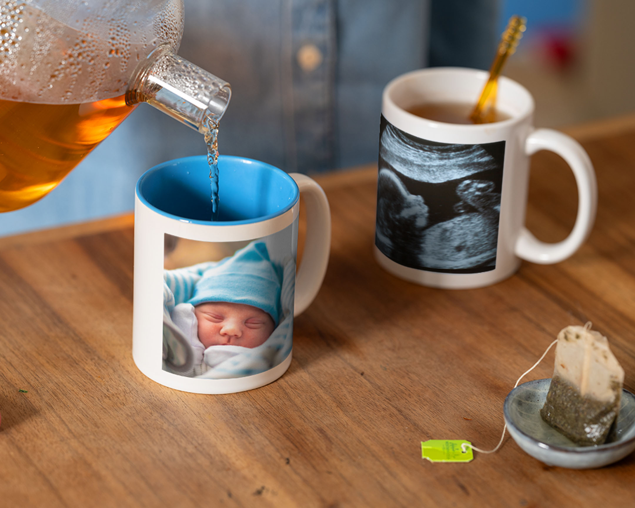 Er wordt thee ingeschonken in een gepersonaliseerde fotomok met een babyfoto, ernaast staat een mok met een echofoto.